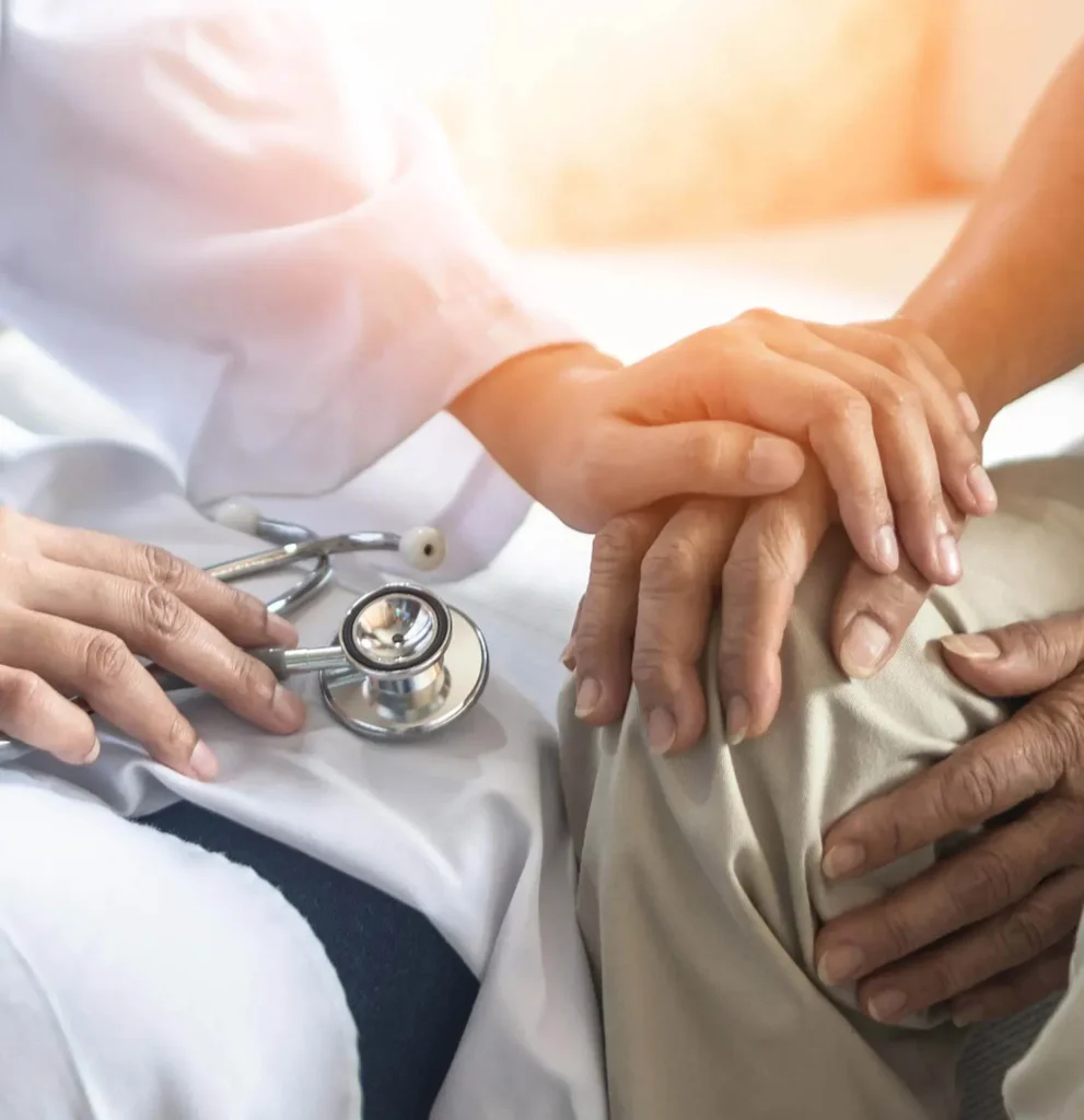 A doctor gently places a hand on top of a patients hand, offering comfort. A stethoscope rests nearby, symbolizing medical care and support.