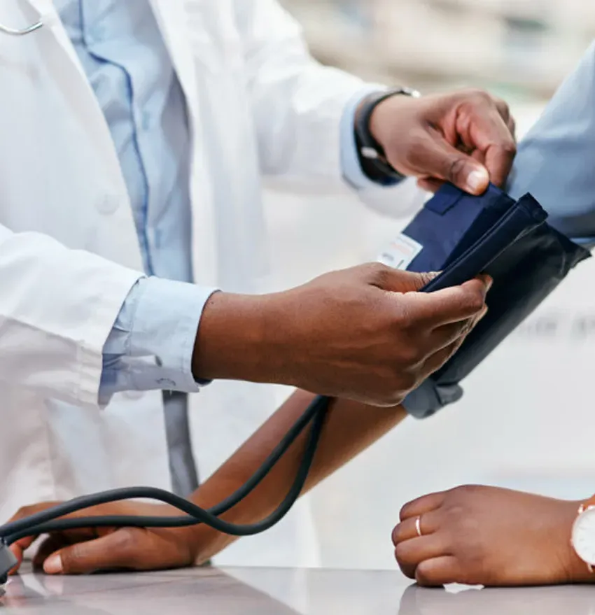 A healthcare professional in a white coat measures a patients blood pressure using a cuff and monitor, focusing on their hands and arms.