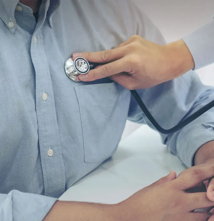 A doctor uses a stethoscope to listen to the chest of a person wearing a light blue shirt during a medical examination.