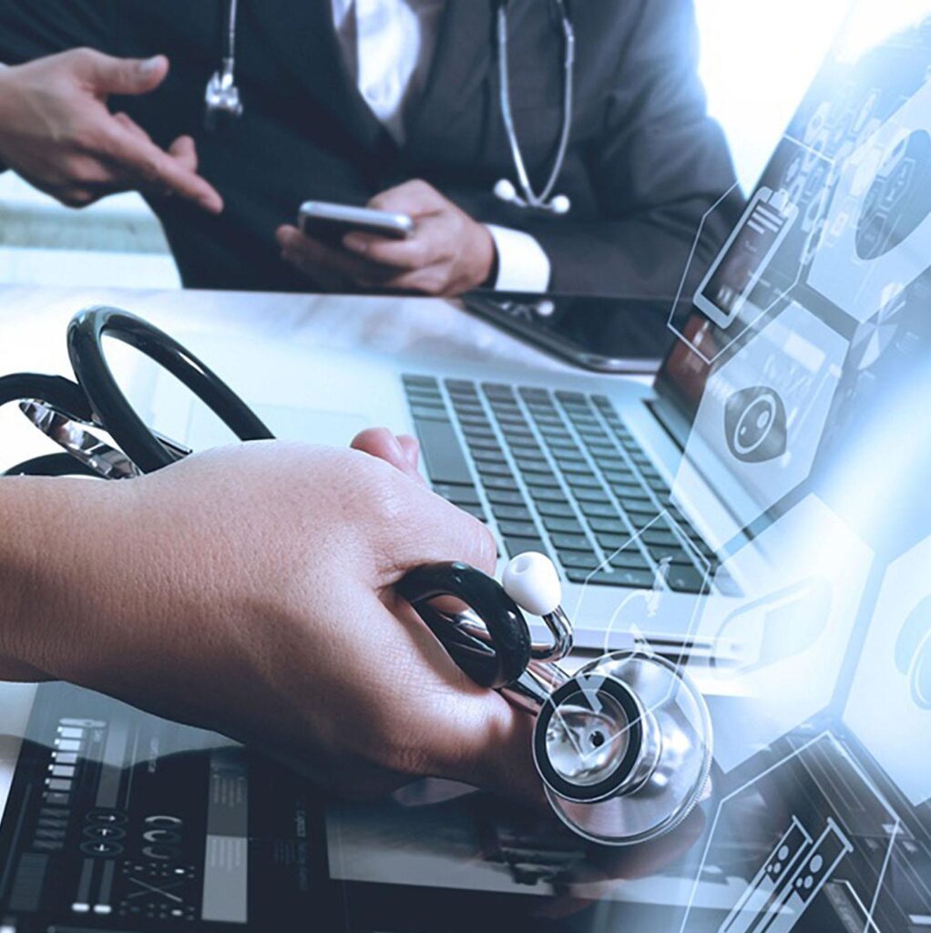 A person holds a stethoscope near a laptop displaying digital medical charts, while another person in a suit gestures in the background, suggesting a discussion about healthcare technology.