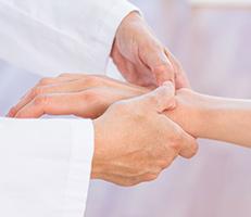 A person in a white coat gently holding and examining another persons hand, suggesting a medical or therapeutic setting.
