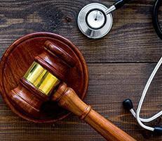 A judge’s wooden gavel and a stethoscope rest on a dark wooden surface, symbolizing the intersection of law and medicine.