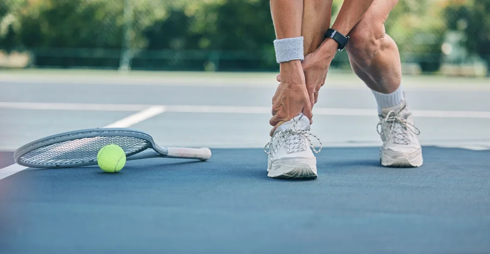 Close up of a tennis player grabbing their ankle in pain from a sports injury.