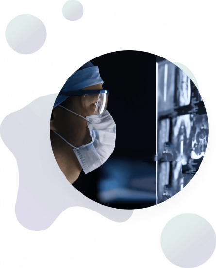 A person wearing a surgical mask, cap, and protective glasses closely examines medical scans displayed on a screen in a dark room. Abstract shapes decorate the background.