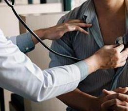 A doctor uses a stethoscope to listen to a patients chest during a medical examination. The patient has unbuttoned their shirt for the checkup.